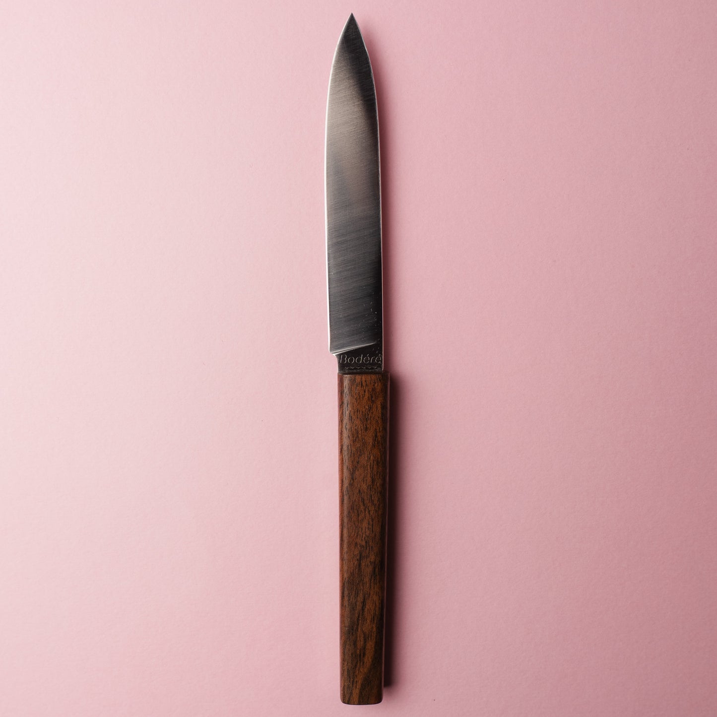 Couteau de table artisanal La Sole par Bodéré, avec manche en bois local de noyer naturel sur fond rose.