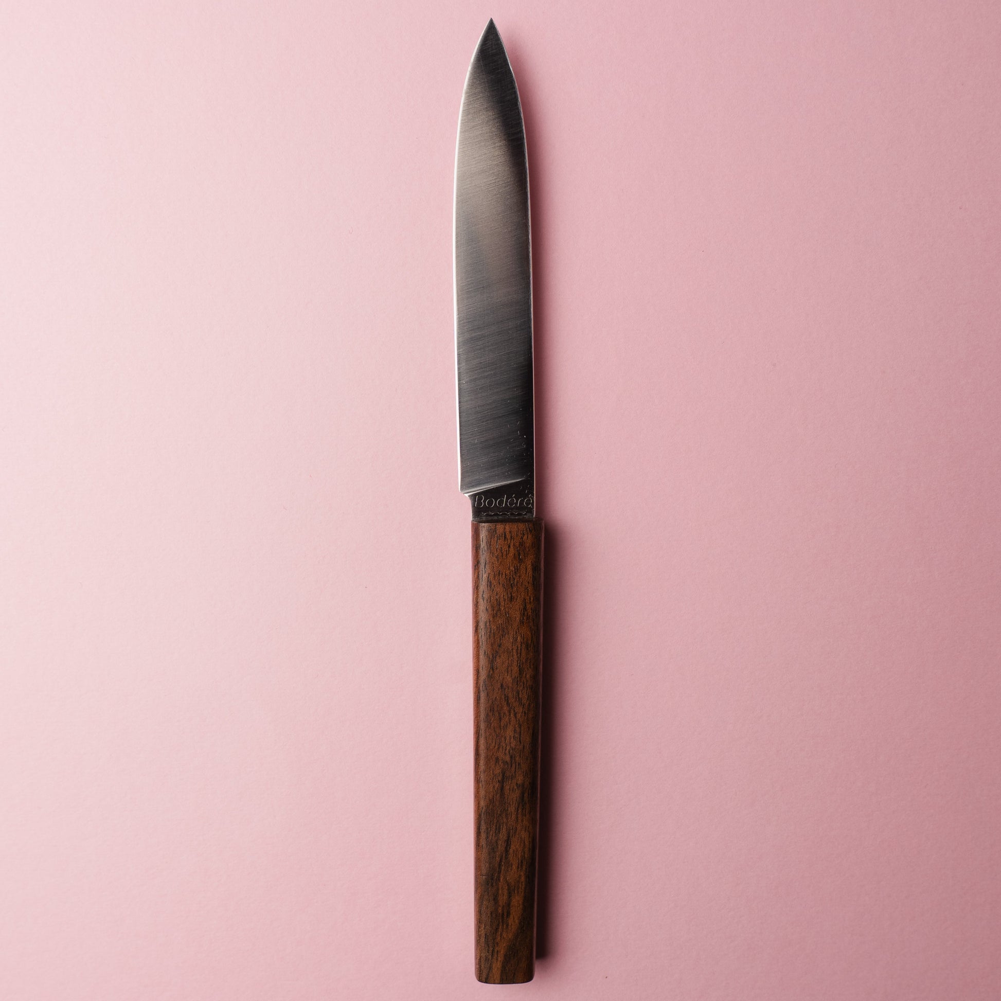 Couteau de table artisanal La Sole par Bodéré, avec manche en bois local de noyer naturel sur fond rose.